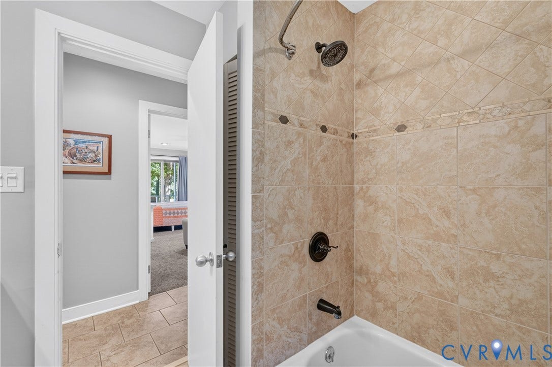 Bathtub with tile surround, dark bronze shower fixture, and a tiled accent border