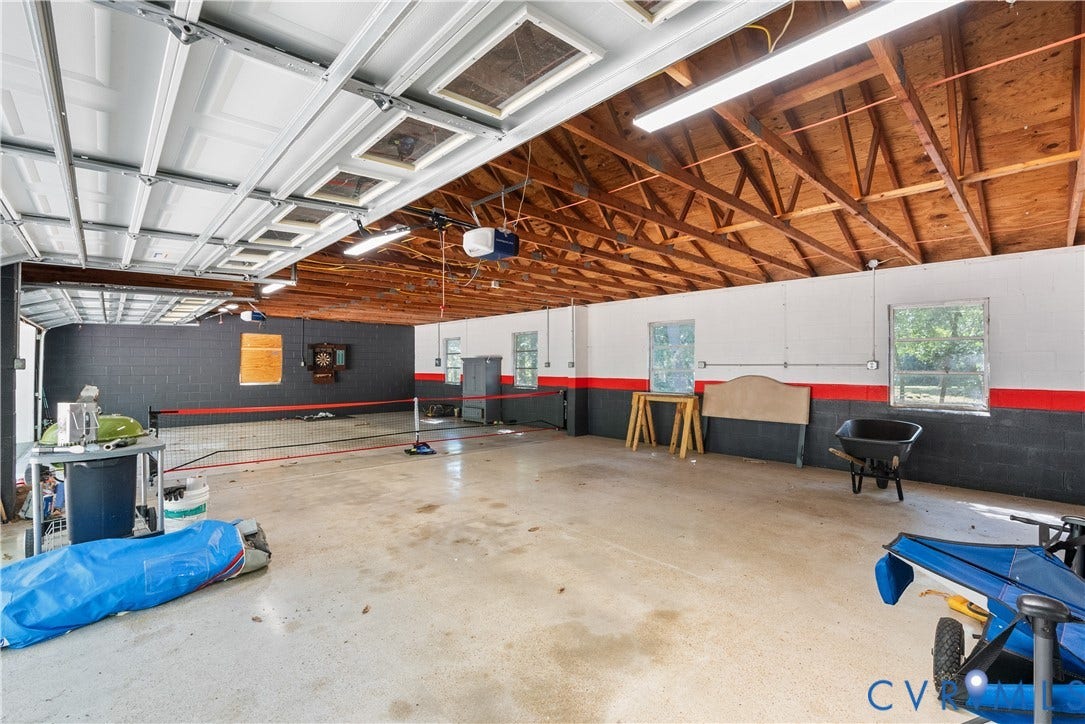 Spacious interior with exposed wood beam ceiling, multiple windows, concrete flooring, and multiple garage doors
