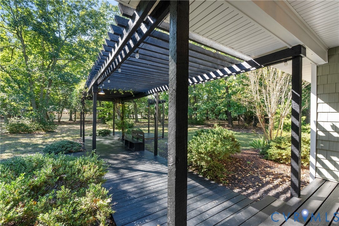 Expansive outdoor decking with a dark finish, integrated pergola, and surrounding mature trees