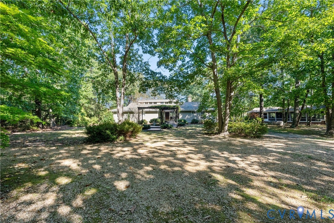 Expansive outdoor space featuring a mature tree canopy, natural ground cover, and a single-story residence with a covered entryway