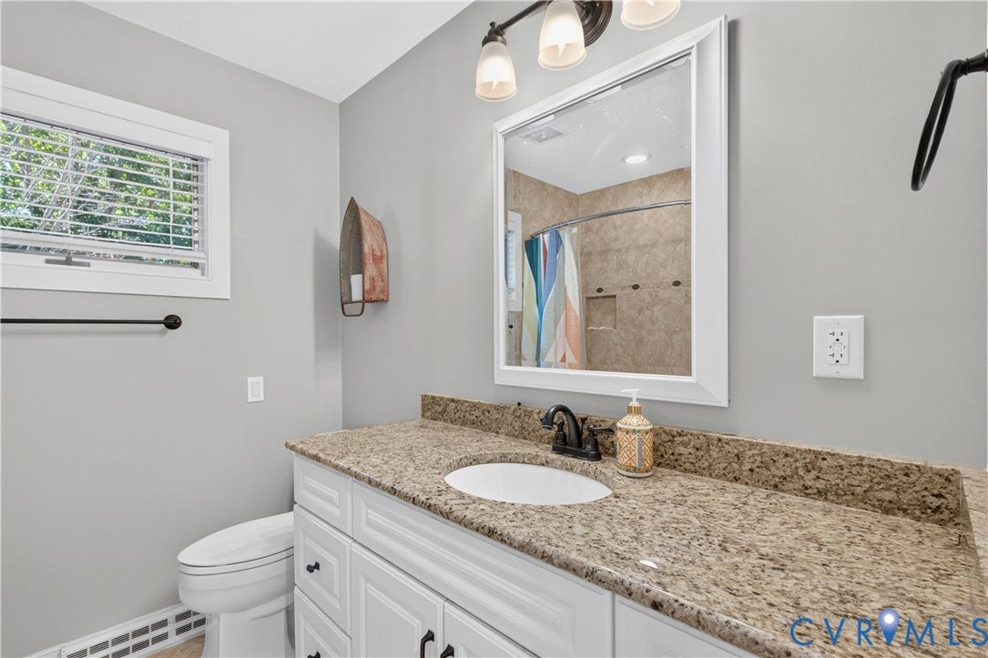 White vanity with built-in oval sink, granite-style countertop, and wall-mounted mirror