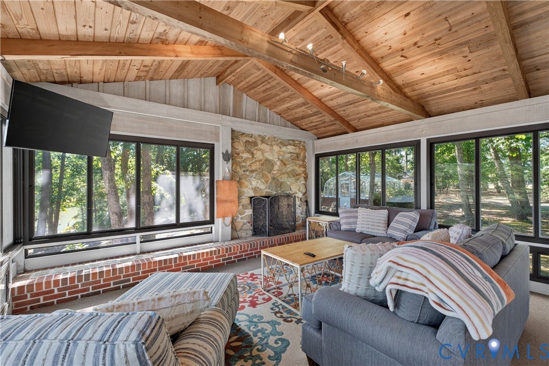 Vaulted wood-paneled ceiling with exposed beams, stone-faced fireplace with hearth, and multiple large windows with black frames