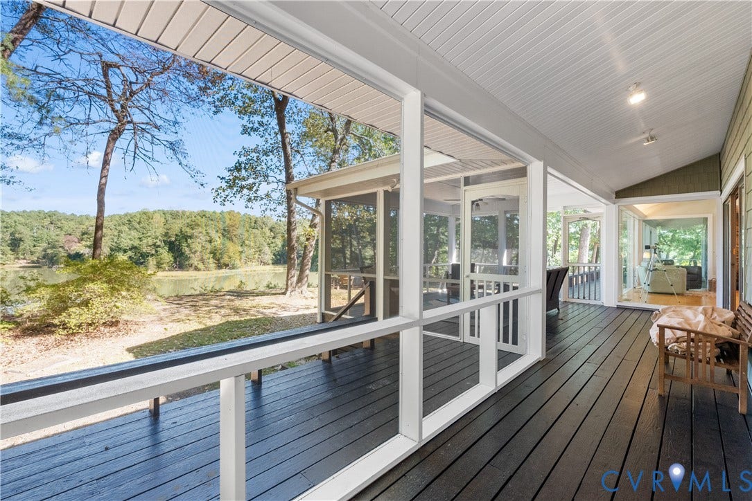Expansive exterior deck with dark wood-finish flooring, screened enclosure, and lakeside scenery