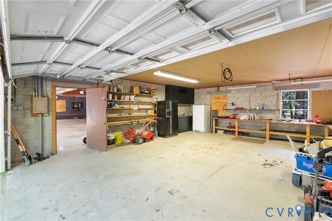 Spacious garage with concrete block walls, overhead garage door, built-in shelving, and a large workbench
