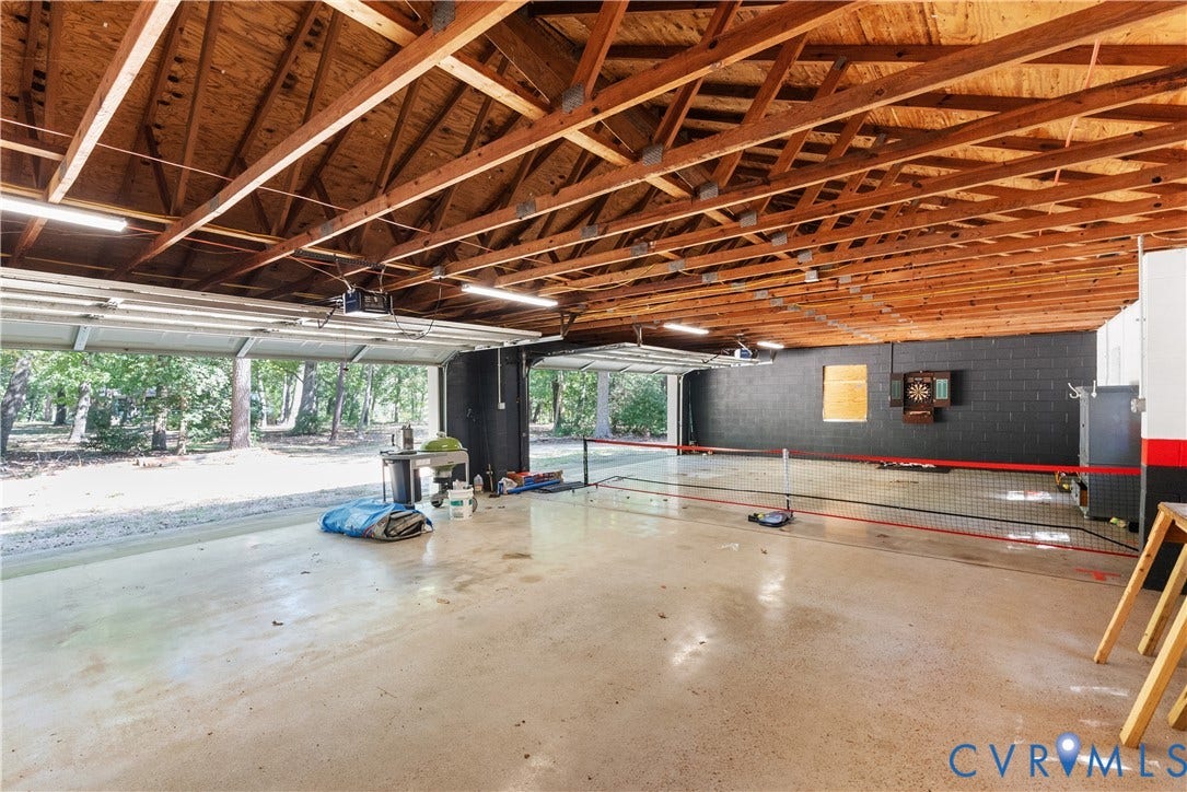 Spacious garage with exposed wood beam ceiling, multiple garage doors, concrete flooring, and ample overhead lighting