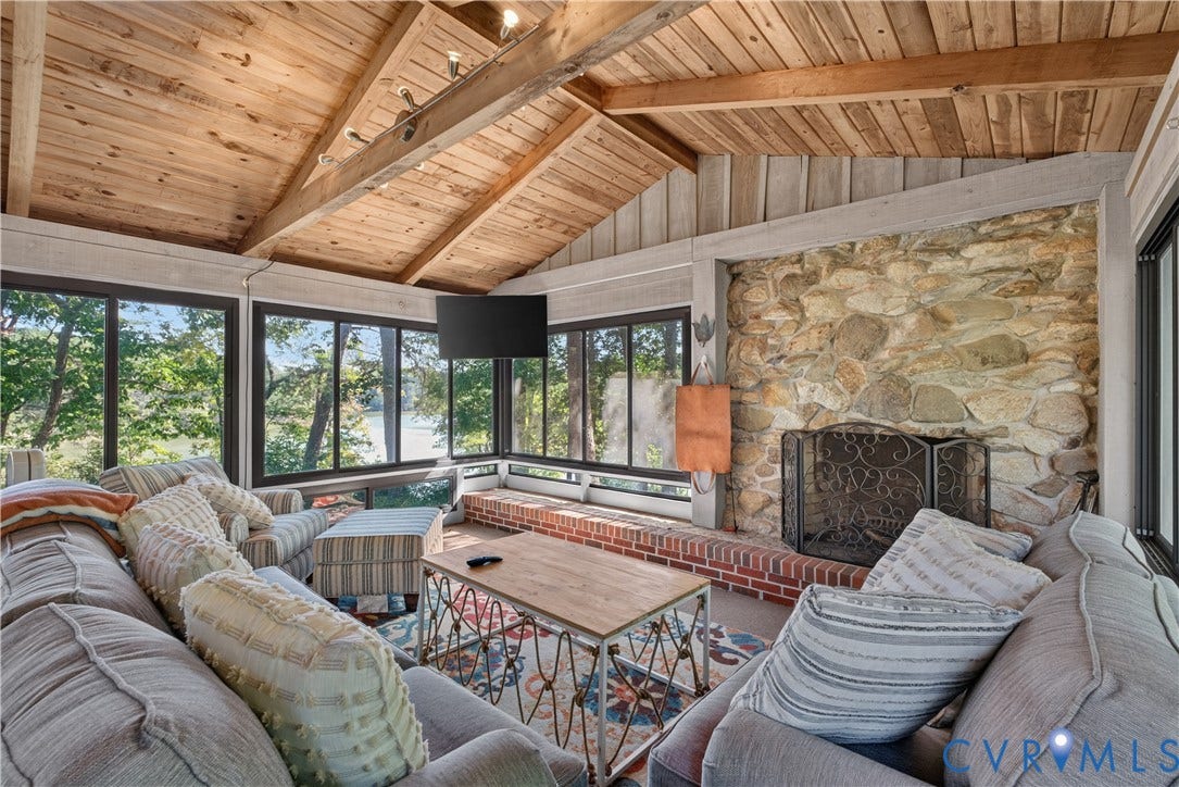 Vaulted wood plank ceiling, stone-surround fireplace with brick hearth, and abundant windows