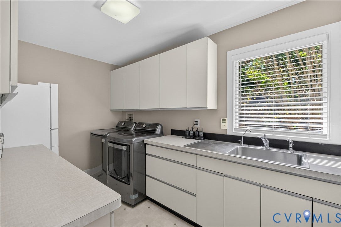Utility room with extensive countertop space, integrated stainless steel sink, ample cabinetry, and natural light from a window