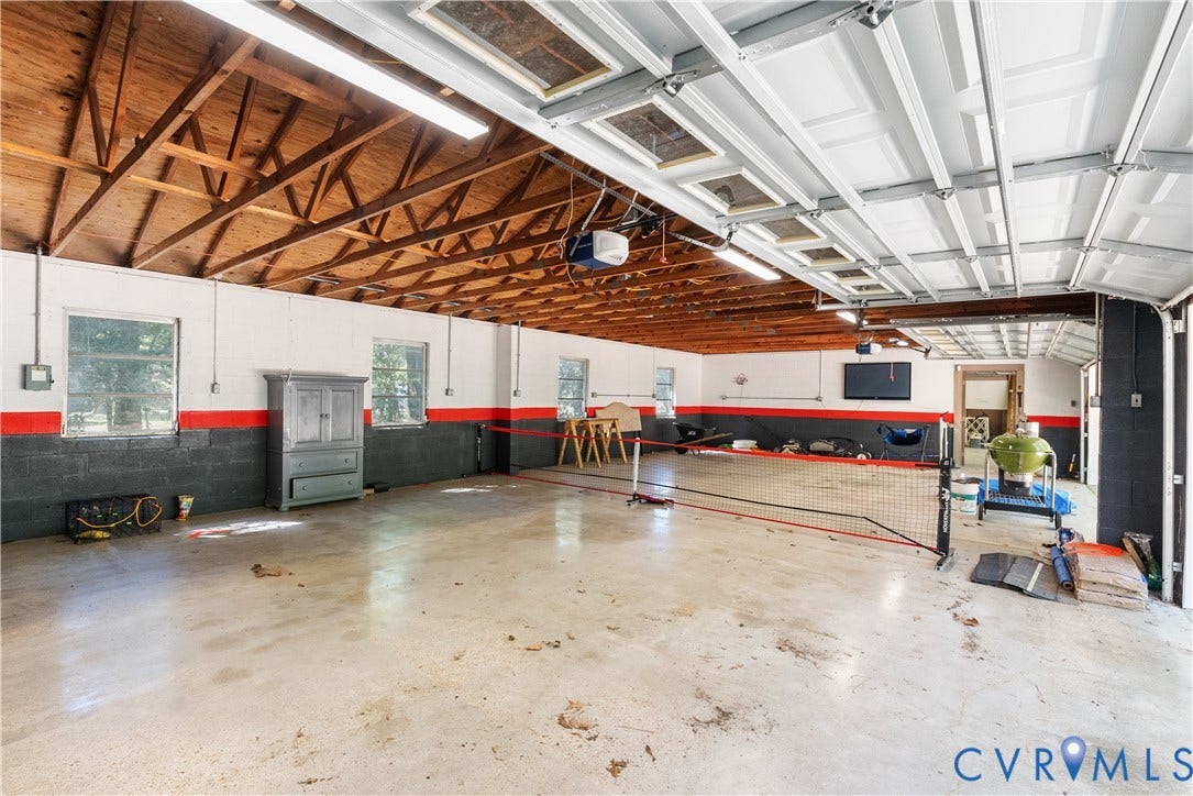 Expansive garage space featuring exposed wood beam ceiling, concrete flooring, multiple windows, and two overhead garage doors