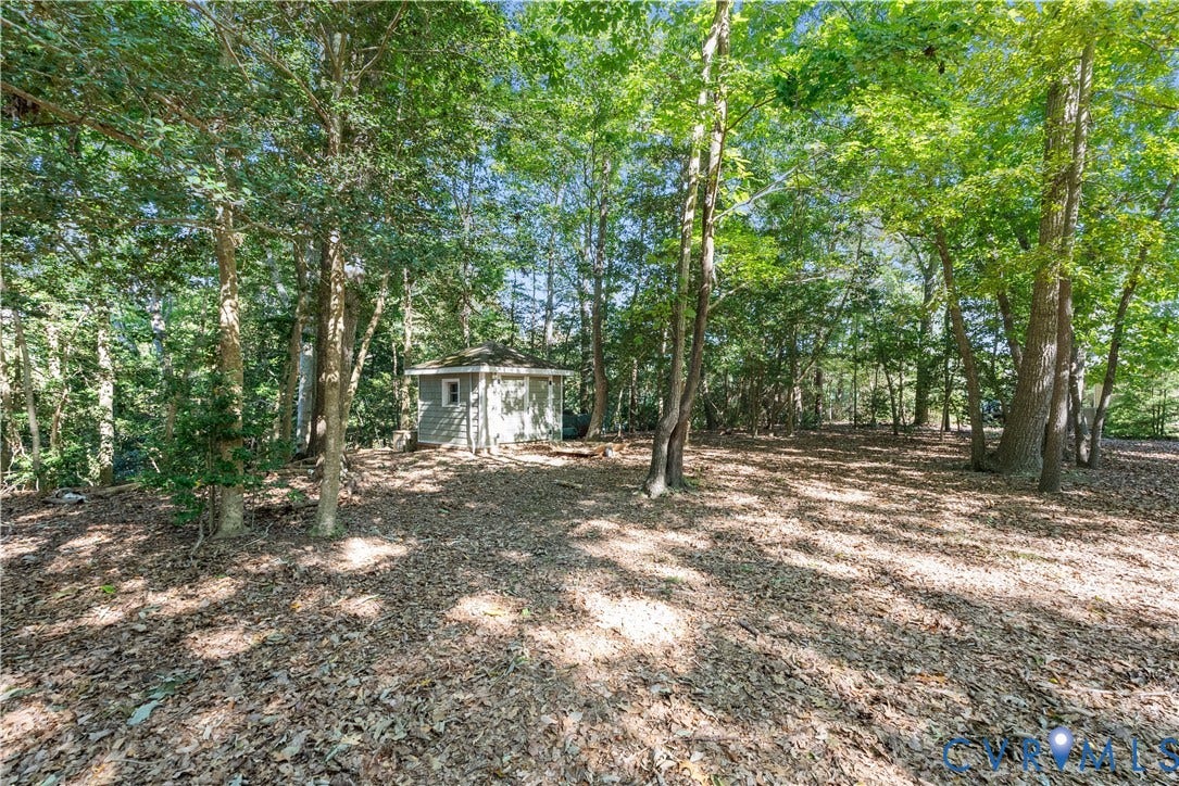 Wooded lot featuring mature trees and a detached shed with siding and a shingled roof