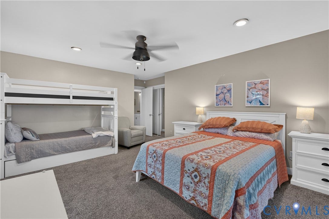 Spacious bedroom suite featuring dual built-in bunk beds with white cabinetry, a queen-size bed with coordinating bedding, dual nightstands with integrated lighting, carpeted flooring, ceiling fan, recessed lighting, and soft neutral wall finishes throughout