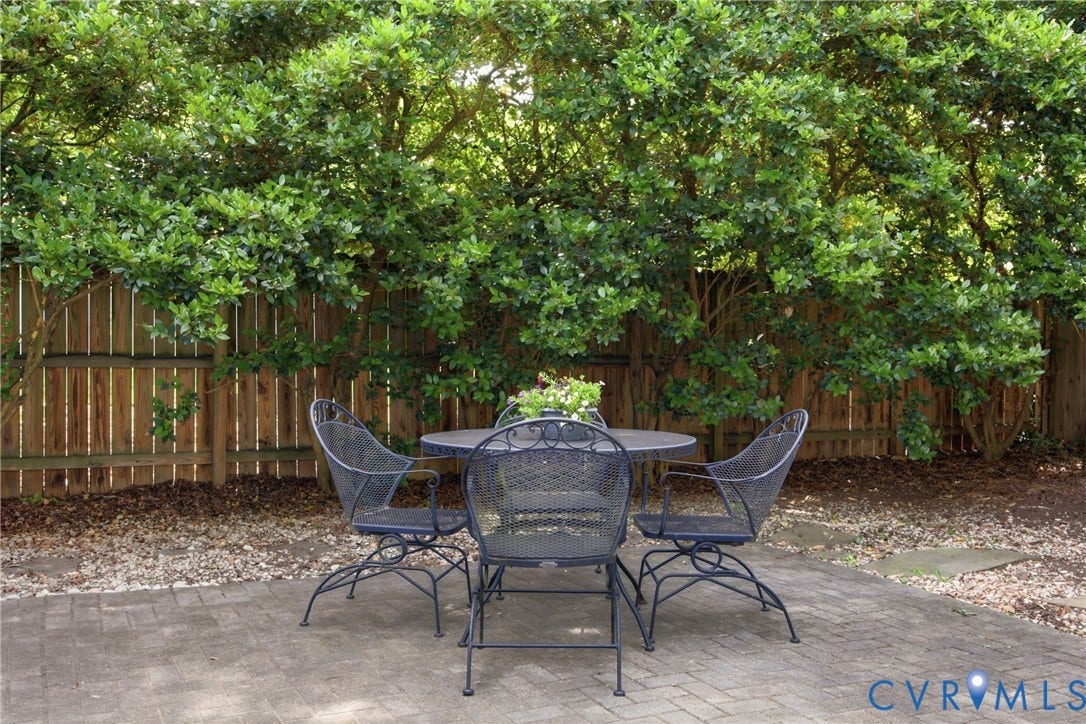 Paved patio area featuring a privacy fence and mature foliage