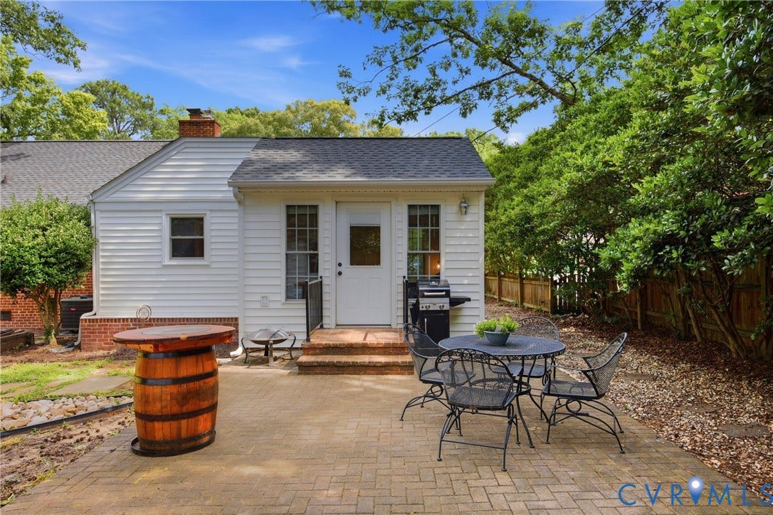Patio with paver flooring, white siding exterior, brick chimney, and mature perimeter landscaping