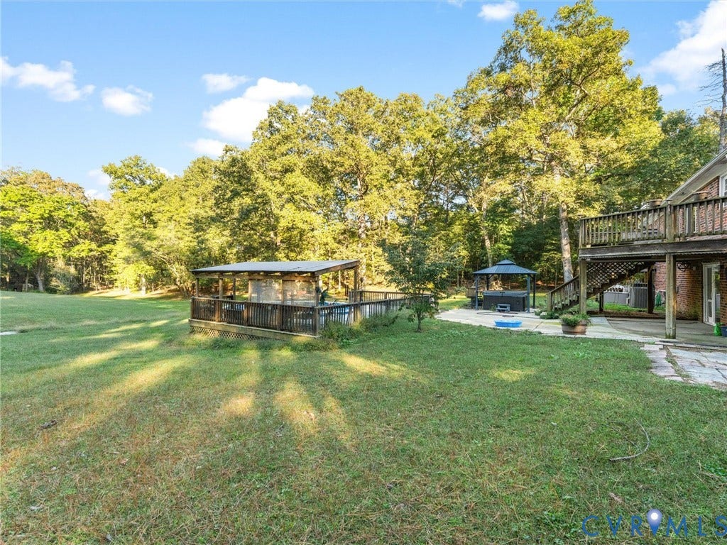 8251 Old Roxbury Road, Quinton, VA 23141 Expansive backyard featuring a tiered wooden deck, stone patio, covered poolside structure, and mature tree line