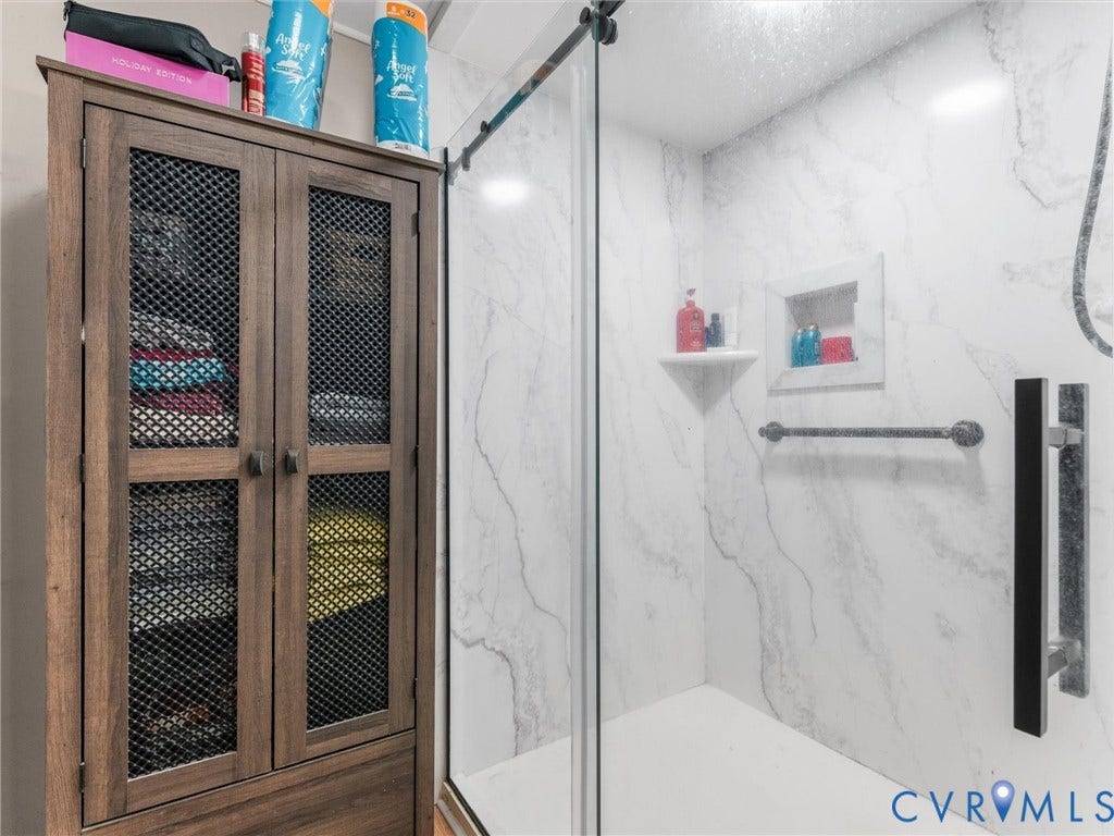 8251 Old Roxbury Road, Quinton, VA 23141 Shower enclosure featuring stone-finish wall panels, a sliding glass door, a built-in recessed wall niche, and an integrated corner shelf