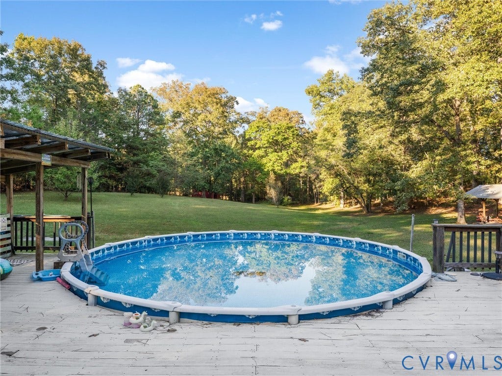 8251 Old Roxbury Road, Quinton, VA 23141 Circular above-ground pool integrated into a wooden deck, featuring a covered patio area and an expansive grass yard framed by mature trees
