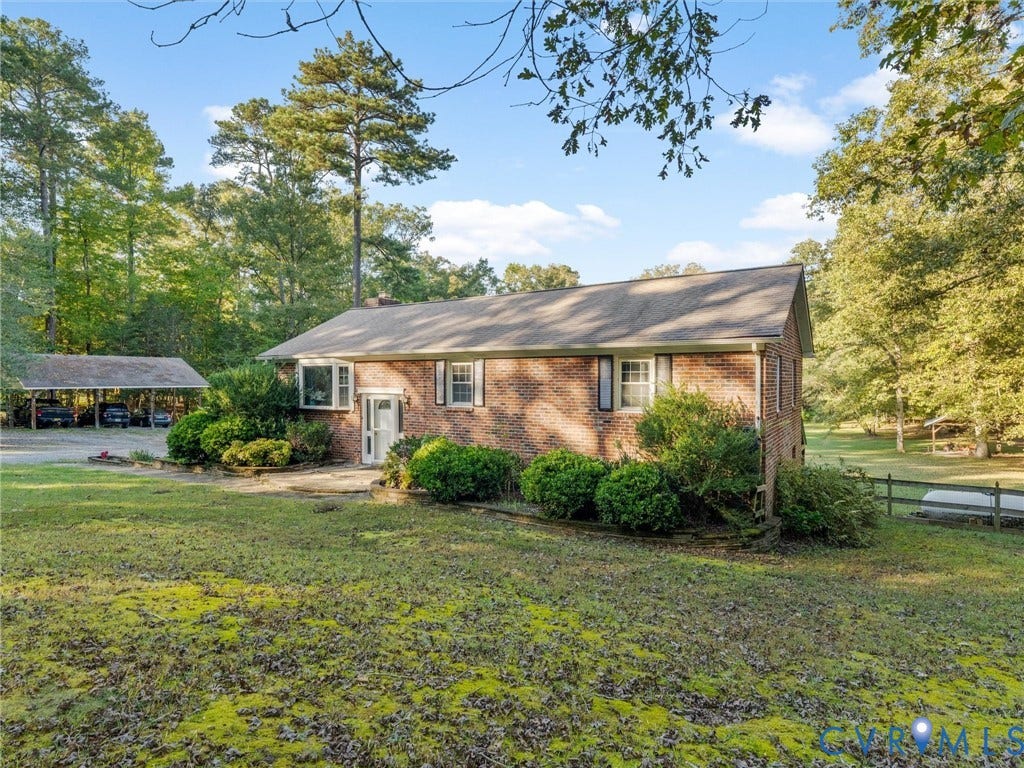 8251 Old Roxbury Road, Quinton, VA 23141 Single-story brick exterior featuring a multi-pitched roof, window shutters, a detached covered carport, and mature tree landscaping
