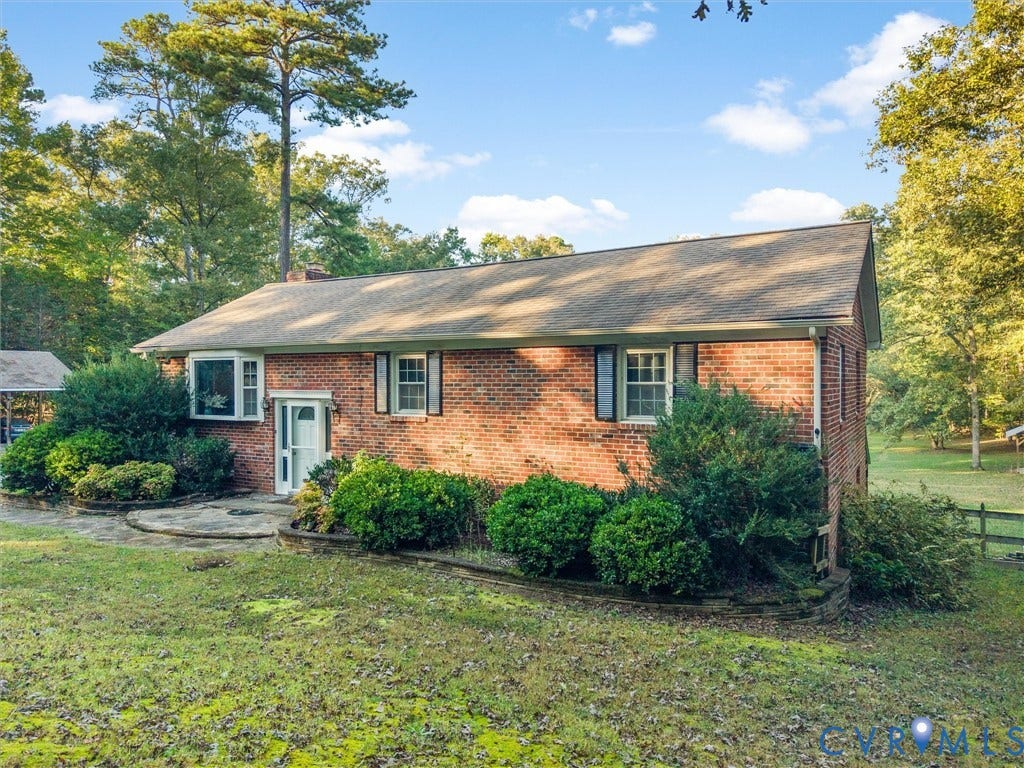 8251 Old Roxbury Road, Quinton, VA 23141 Red brick exterior featuring a multi-gable roofline, bay window, stone patio, and mature perimeter landscaping
