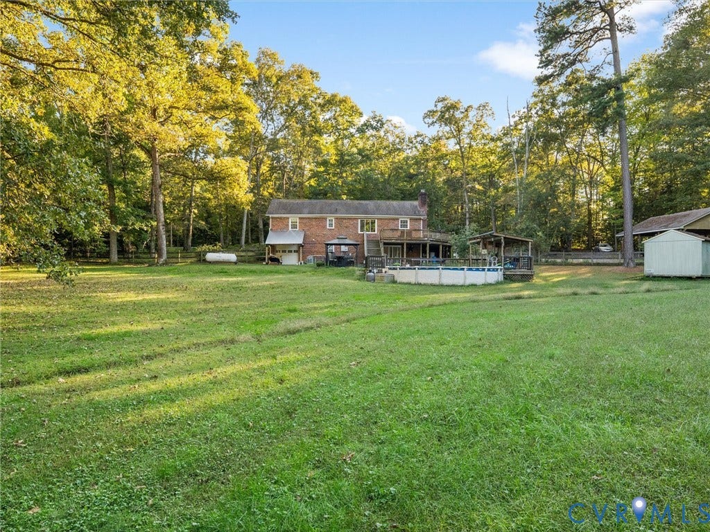 8251 Old Roxbury Road, Quinton, VA 23141 Expansive grounds featuring a brick exterior, elevated wood deck, above-ground pool, and detached storage structure surrounded by mature trees