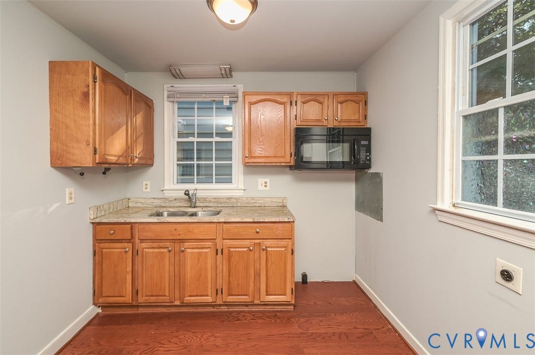 Kitchenette featuring wood-finish cabinetry, granite-style countertops, an undermount double basin sink, and wood-finish flooring