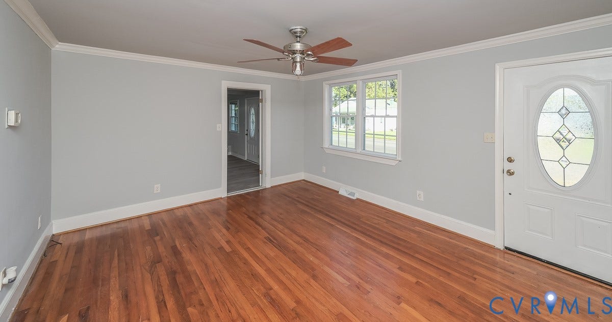 Hardwood flooring, light gray wall paint, white trim, ceiling fan with wood-finish blades, and a front door with decorative glass inserts