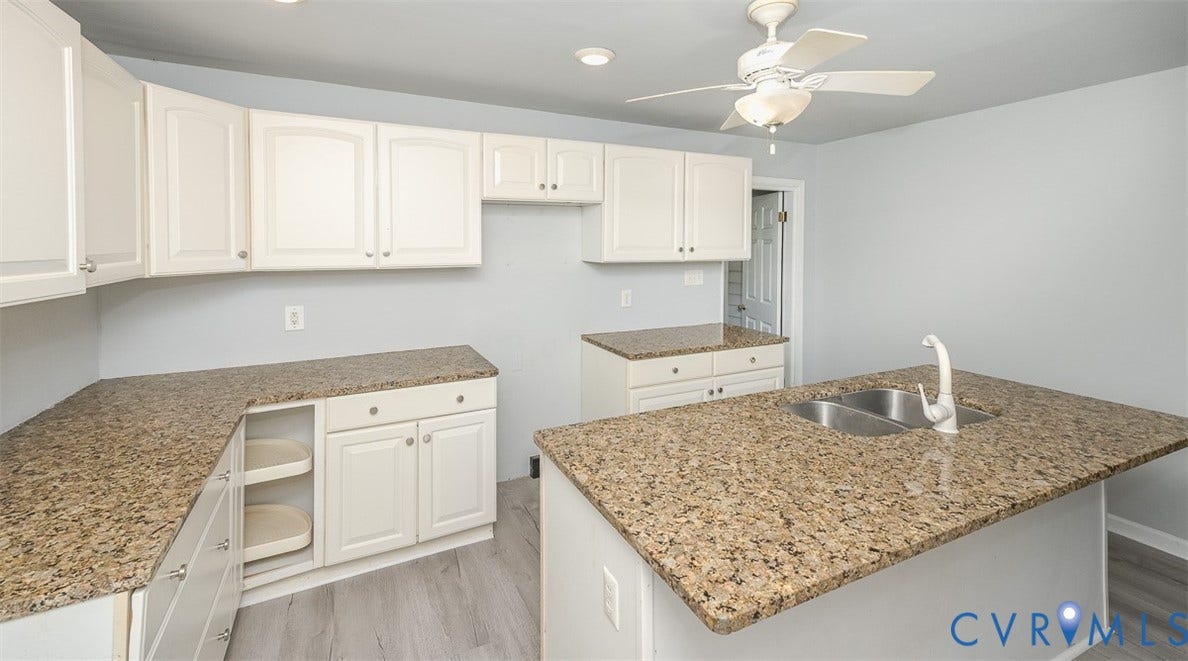 Kitchen with white cabinetry, speckled countertops, stainless steel double basin sink, and wood-finish flooring