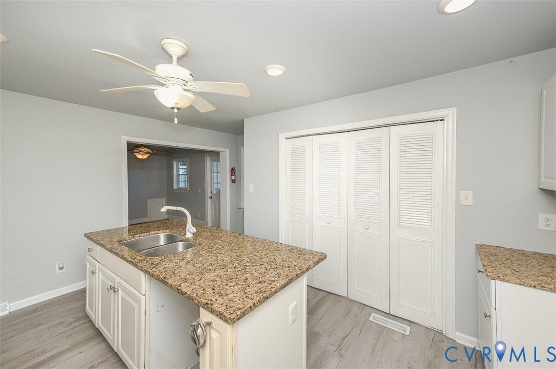 Kitchen island with dual basin sink, granite countertop, and white cabinetry