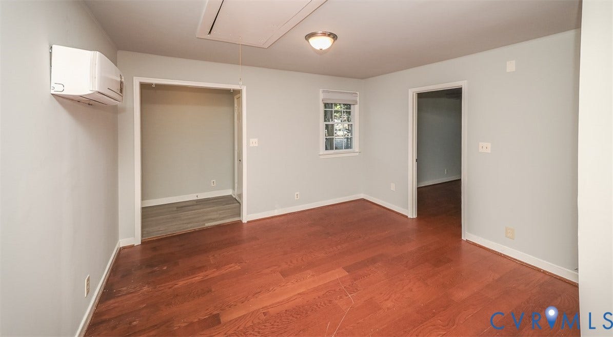 Hardwood flooring, light gray wall paint, white trim, ceiling-mounted light fixture, and a wall-mounted AC unit
