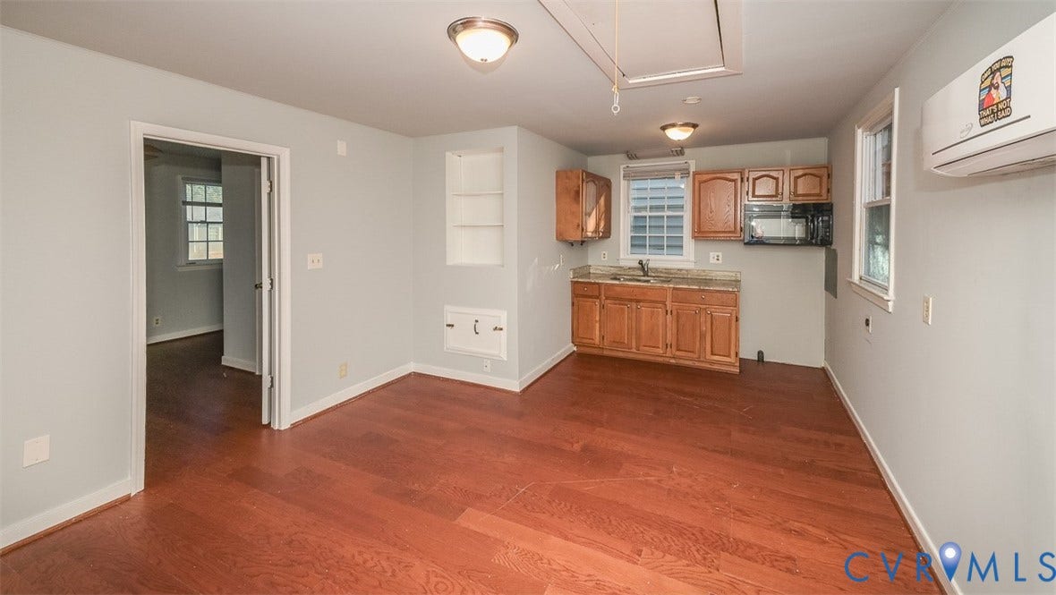 Wood-finish flooring throughout, light gray wall paint, kitchen area with wood cabinetry, light-colored countertops, and a built-in microwave