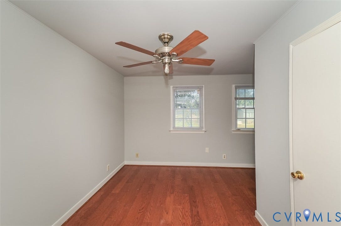 Wood-finish flooring, light grey wall paint, two windows, and a ceiling fan with integrated lighting