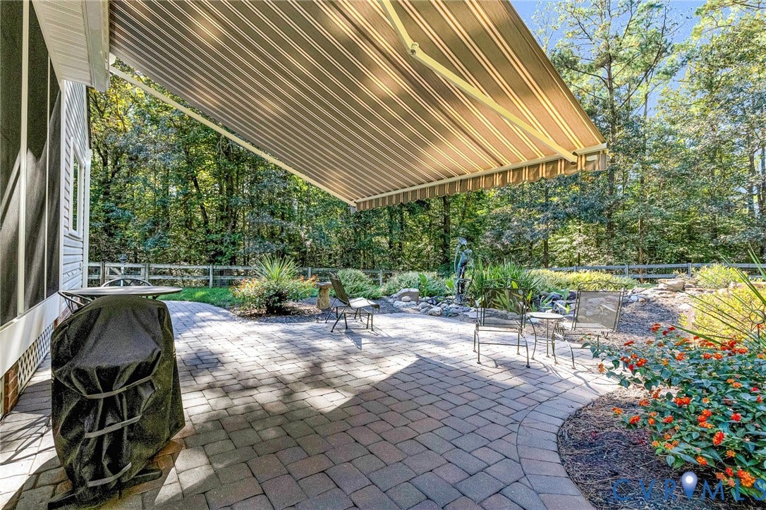 360 Laurel Drive, Aylett, VA 23009 Patio featuring a retractable awning, paver stone hardscaping, natural rock landscaping, and mature perimeter trees