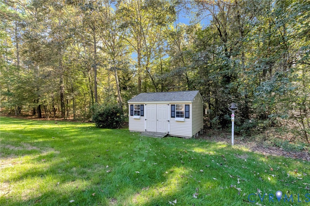 360 Laurel Drive, Aylett, VA 23009 Freestanding storage shed with dual doors, functional windows with shutters, and a window box, situated on a grassy area with mature trees forming a natural perimeter