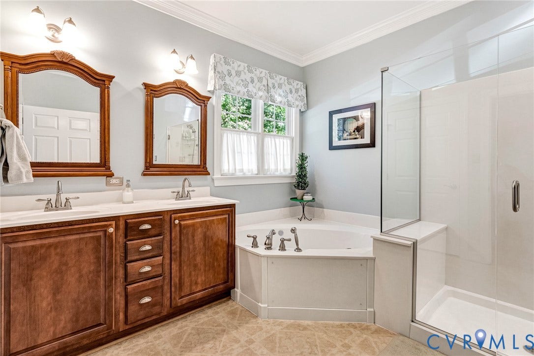 360 Laurel Drive, Aylett, VA 23009 Dual sink vanity with wood-finish cabinetry, corner soaking tub, separate glass-enclosed shower, and a large window
