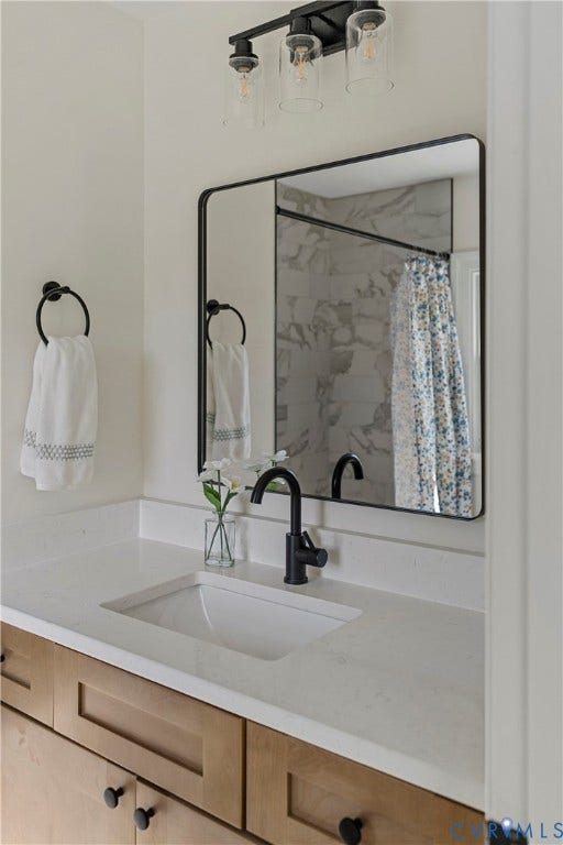 2601 Greenway Avenue, Lakeside, Henrico, VA 23228 Modern bathroom vanity featuring light wood-finish cabinetry, a white countertop with an integrated basin, a matte black faucet, and a rectangular mirror with a black metal frame