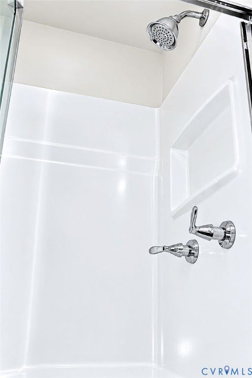 Shower enclosure featuring a chrome showerhead, integrated shelf, and chrome fixtures