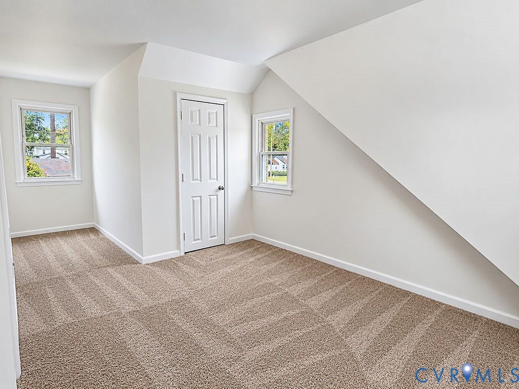 Room featuring neutral tone carpet, white painted walls, two windows, and a paneled door