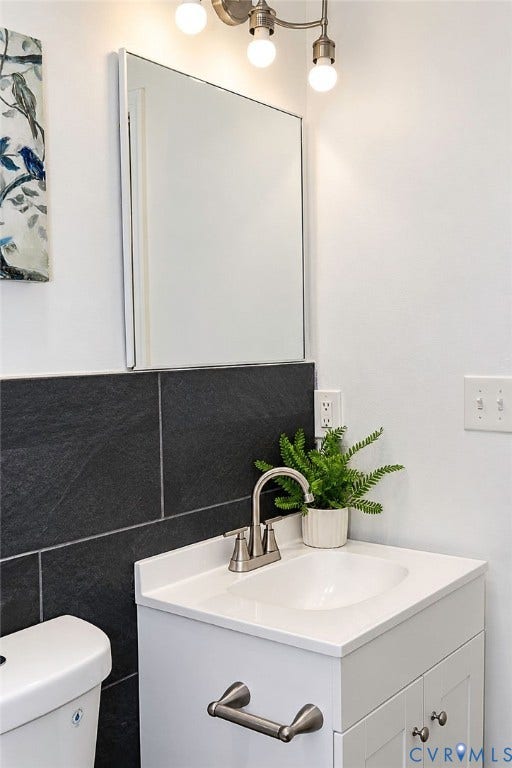 Vanity with integrated sink, brushed nickel faucet, wall-mounted mirror, and dark tile wainscoting