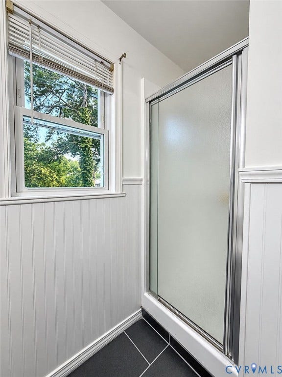 Frosted glass shower enclosure, beadboard wall paneling, tile flooring, and a double-hung window