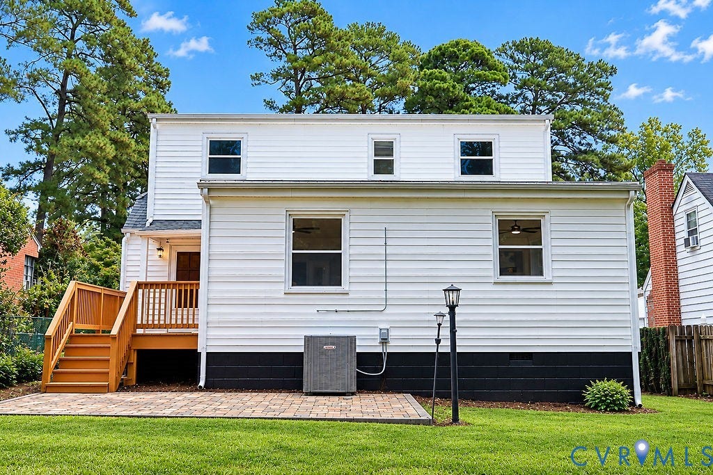 Rear exterior featuring white horizontal siding, a wood-finish deck with stairs, a brick paver patio, and a grass lawn