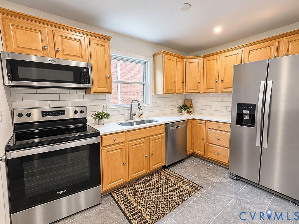 Stainless steel appliances, light wood cabinetry, white countertops, subway tile backsplash, and grey tile flooring