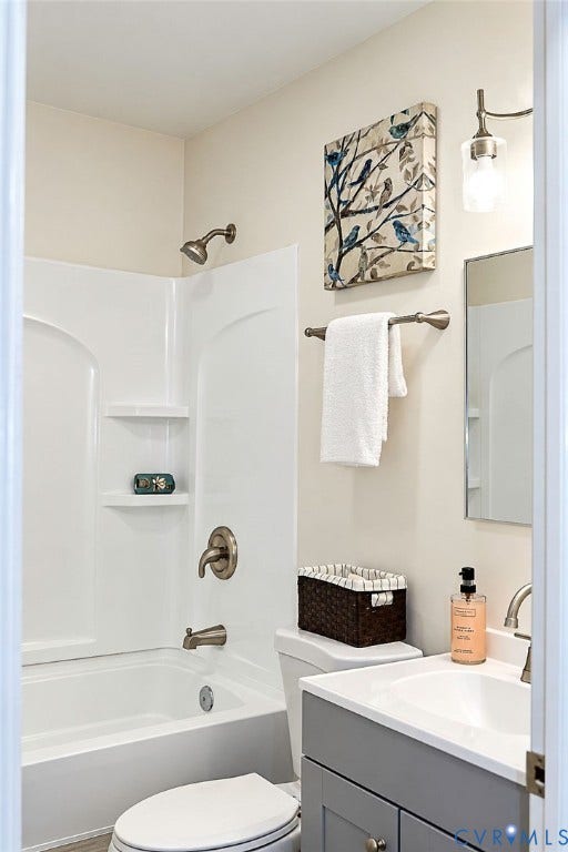 Bathtub with integrated shower, brushed metal fixtures, vanity with gray cabinetry, white countertop with integrated sink, wall-mounted light fixture