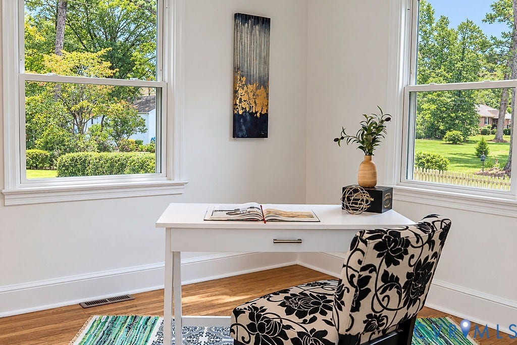 Bright home office bathed in natural light from dual large windows overlooking mature landscaping