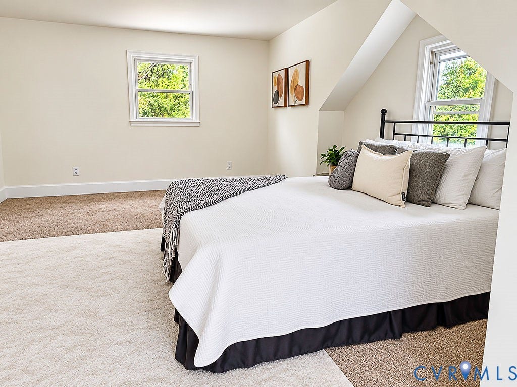 Warm neutral wall paint, sloped ceiling detail, two distinct window openings, and neutral carpeting