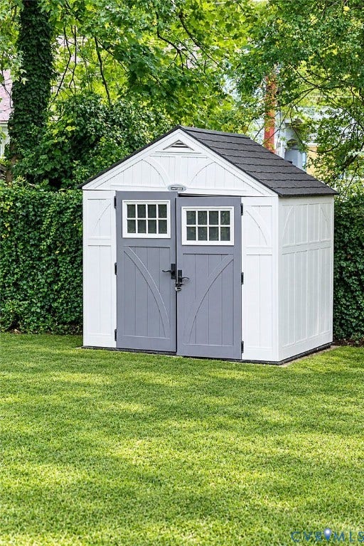 Gable roof storage shed featuring double doors with window panes, a peaked roof, and a low-maintenance exterior, set on a manicured lawn