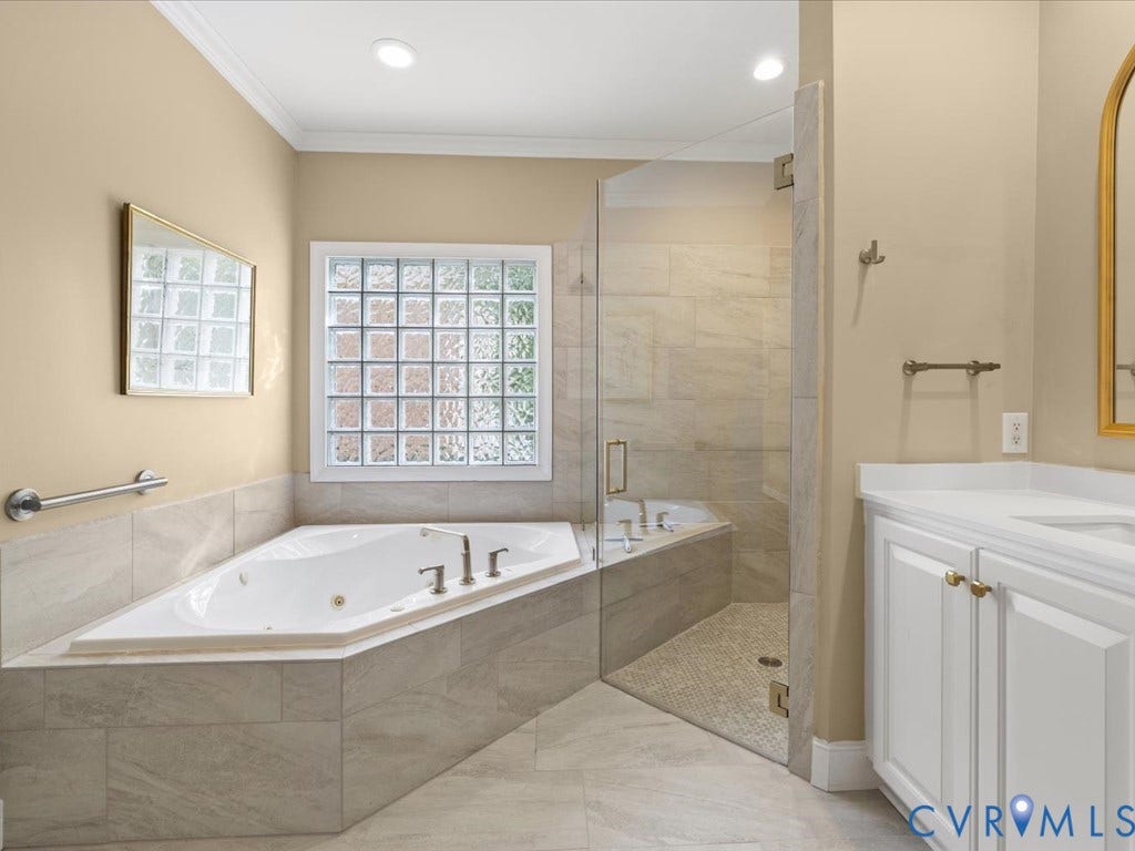 12126 Club Commons Drive, Club Commons, Glen Allen, VA 23059 Corner jetted soaking tub, glass block window, frameless glass shower enclosure, single vanity with white cabinetry, and a light-toned tile floor