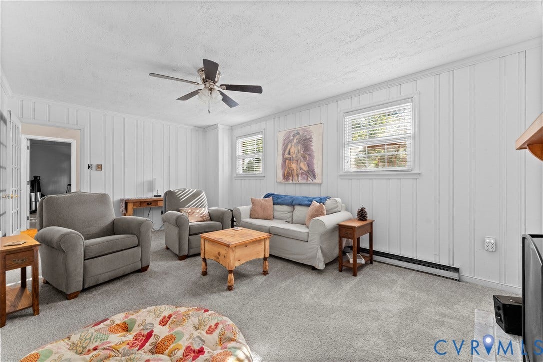 109 Webster Road, Sandston, VA 23150 Carpeted living space featuring board and batten wall paneling, ceiling fan, and multiple windows with blinds