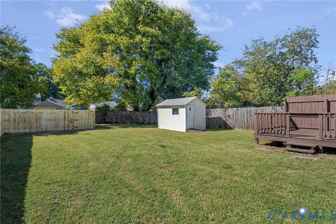 5304 Gillespie Avenue, Henrico, VA 23228 Expansive backyard featuring a white storage shed, a wood-stained deck, a newly installed wood fence, and mature trees