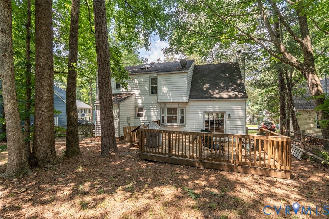 Expansive rear wooden deck, white siding exterior, multiple mature trees, and a visible chimney structure