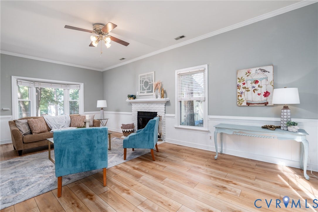 Light wood-finish flooring, white crown molding, and a brick fireplace with a white mantel