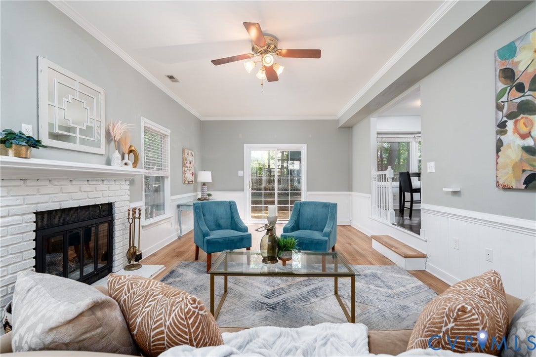 Living area featuring a painted brick fireplace, wood-finish flooring, white crown molding, and a ceiling fan with integrated lighting.