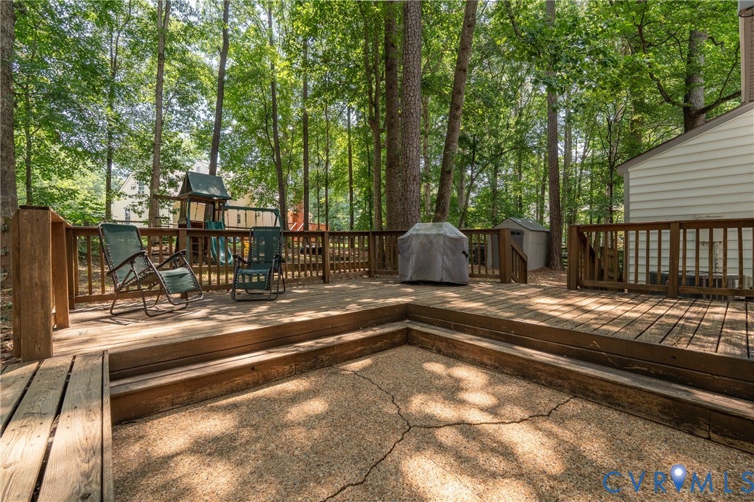 Expansive wood deck with a two-tier design, complementing a concrete patio area, and surrounded by mature trees
